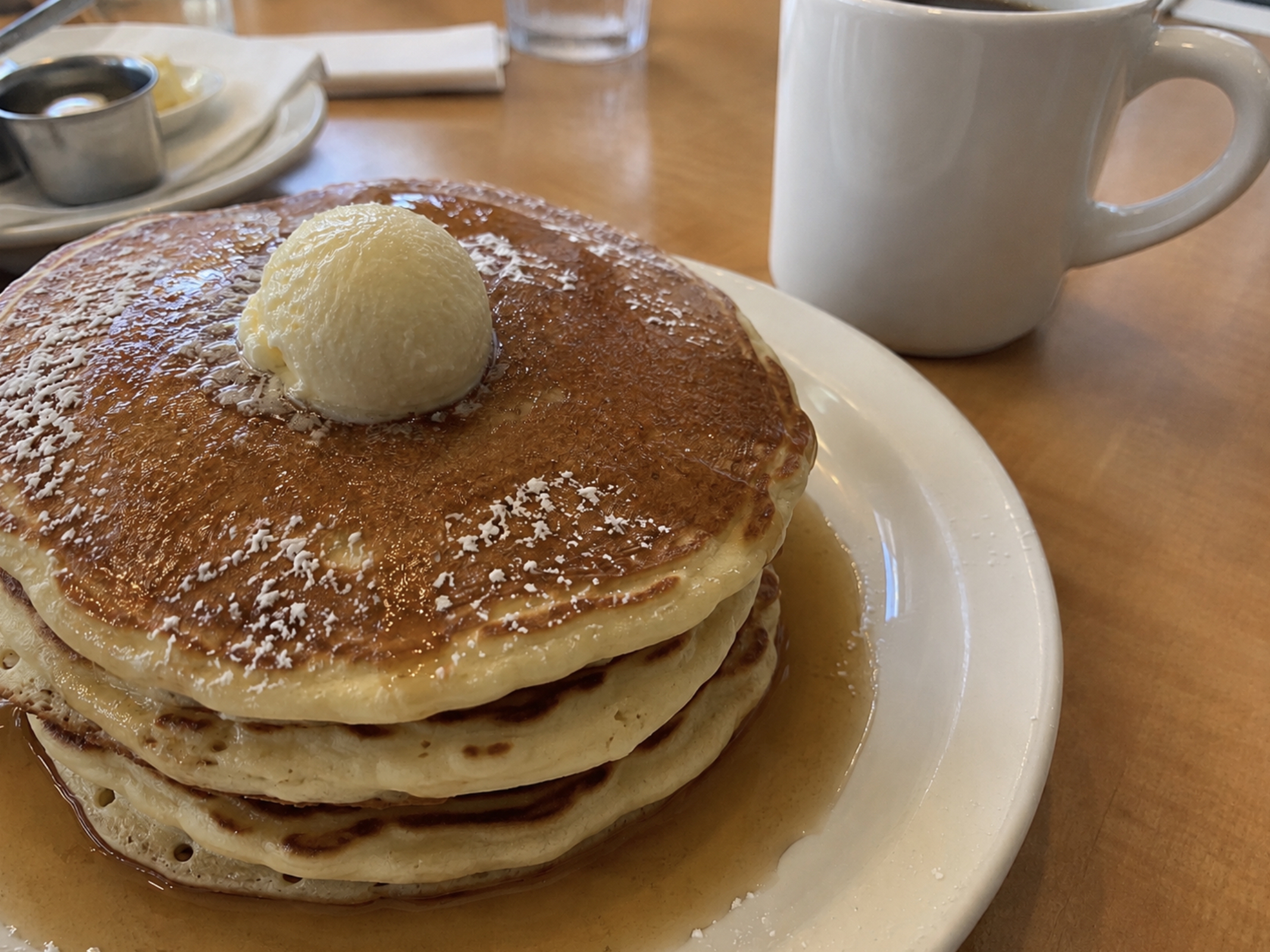 stack of pancakes sitting on a table at a restaurant with a cup of coffee